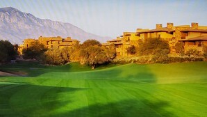 A golf course with a mountainous backdrop and traditional-style buildings.