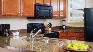 A kitchen with wooden cabinets, a black microwave, a stove, a sink, and a bowl of lemons.