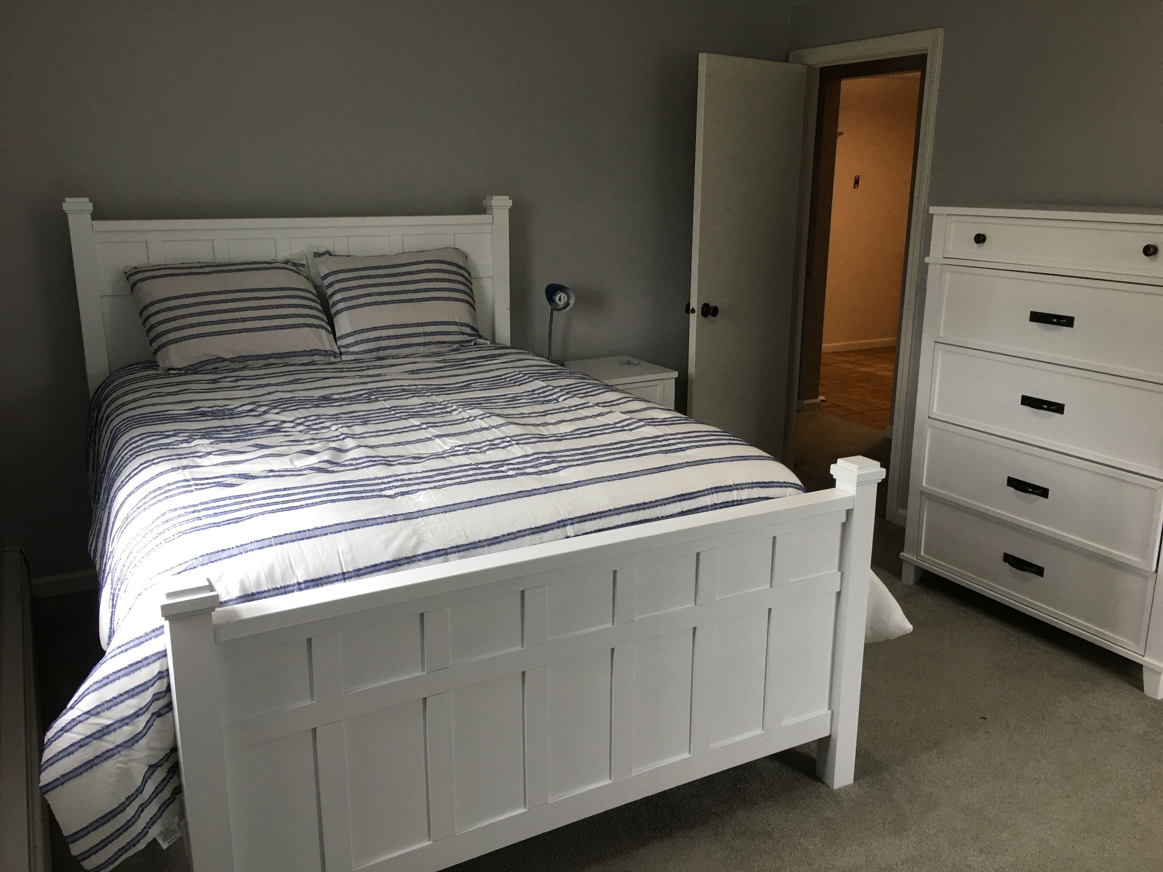 A white bed with striped bedding, a nightstand, and a white dresser with drawers.