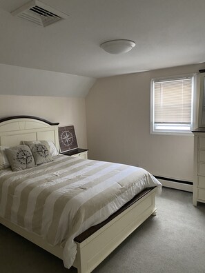 A bedroom with a bed, a nightstand, a window with blinds, and a ceiling vent. - WALK TO BEACH- NEWLY RENOVATED (Narragansett)