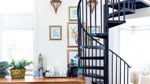 A modern interior with a spiral staircase, a wooden table with decorative items, a wicker sofa, and a colorful rug. - The Farmhouse at Veritas (Afton)