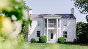 A two-story white house with a central entrance, columns, and a symmetrical facade. - The Farmhouse at Veritas (Afton)