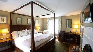 A four-poster bed with a wooden frame, a bedside table with a lamp, a dresser, and a mirror on the wall.