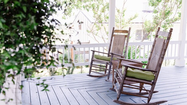 A wooden porch with two rocking chairs and a white fence. - The Farmhouse at Veritas (Afton)