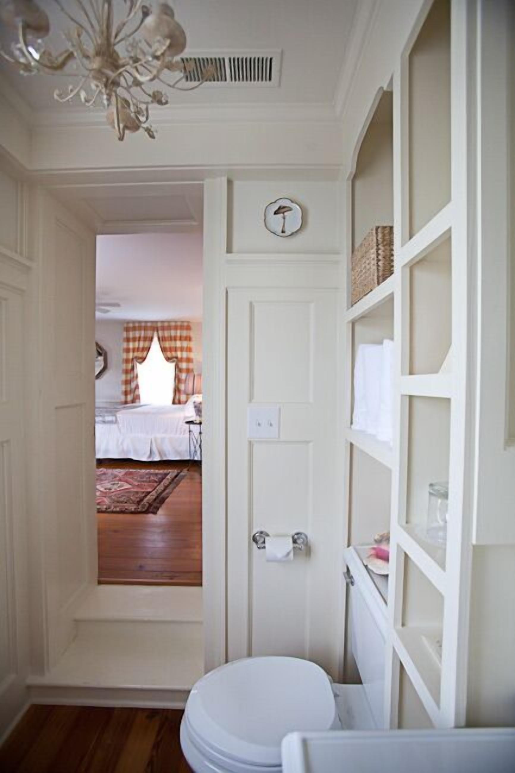 Un estrecho pasillo que conduce a un dormitorio con cama y ventana con cortinas a cuadros.