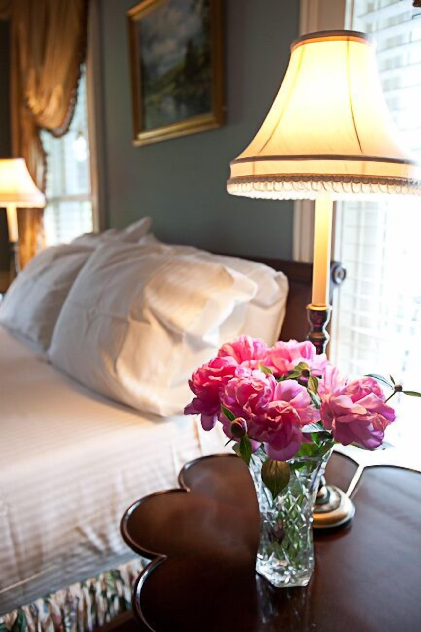 A hotel room with a bed, a bedside table with a vase of flowers, and a lamp.
