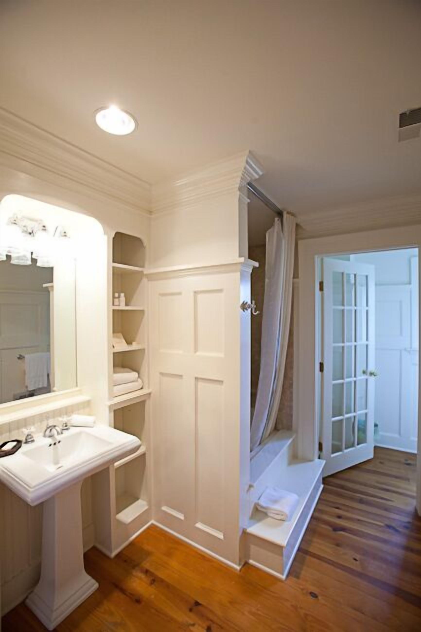 A bathroom with a pedestal sink, a vanity mirror, and a shower area with a curtain.