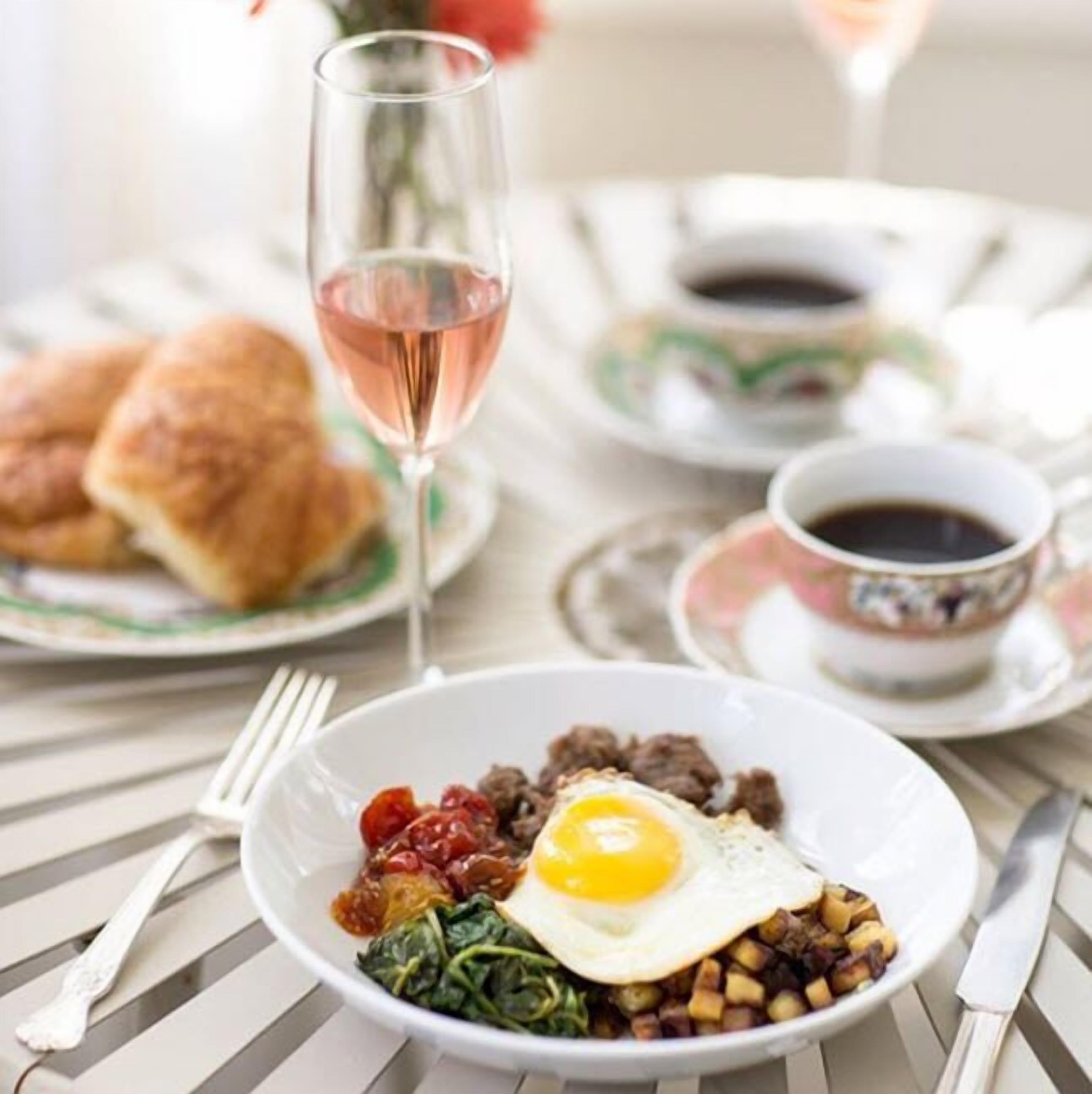 A breakfast setting with a plate of eggs, greens, and potatoes, a glass of pink drink, and a cup of coffee on a table.