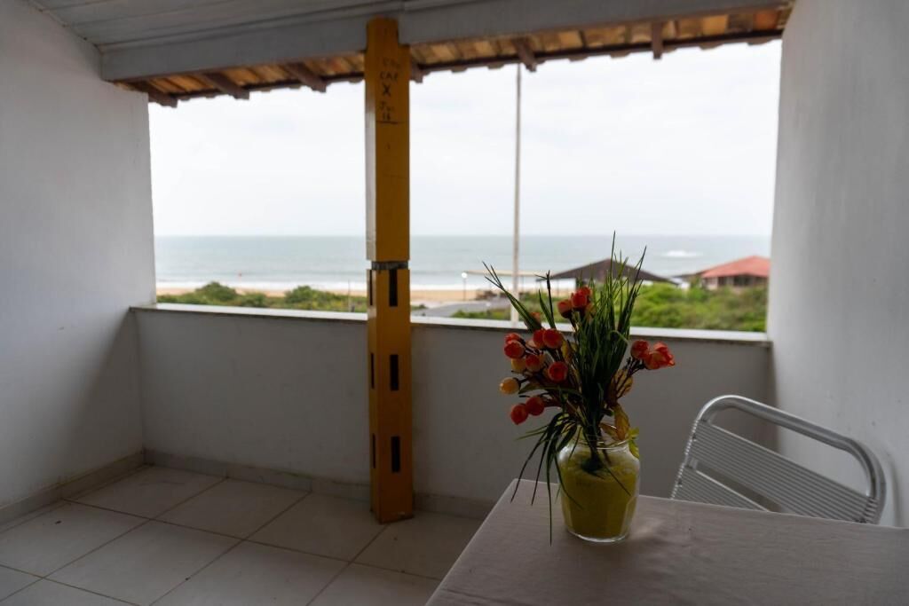 A balcony with a view of the beach, a table with a vase of flowers, and a chair.
