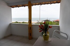 A balcony with a view of the beach, a table with a vase of flowers, and a chair.