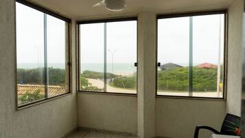 Quarto com grandes janelas que oferecem vista para o mar e vegetação.