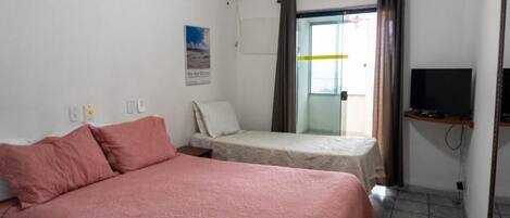A hotel room with a bed, a small table, a television, and a window with curtains.