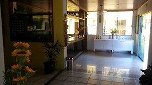 A hallway with a tiled floor, a reception desk, a white counter, and a potted plant. - Pousada Girassol (Rio das Ostras)