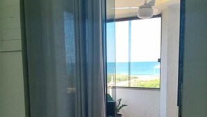 A room with a sliding glass door leading to a balcony with a view of the sea. - Pousada Girassol (Rio das Ostras)