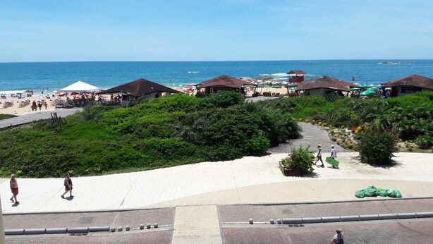 A beachside resort with a paved walkway, beach umbrellas, and beach huts. - Pousada Girassol (Rio das Ostras)