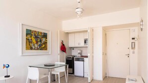 A compact kitchen with white cabinets, a microwave, and a stove. There is a dining table with two chairs and a framed painting on the wall. - Luminoso Duplex en Recoleta (Buenos Aires)