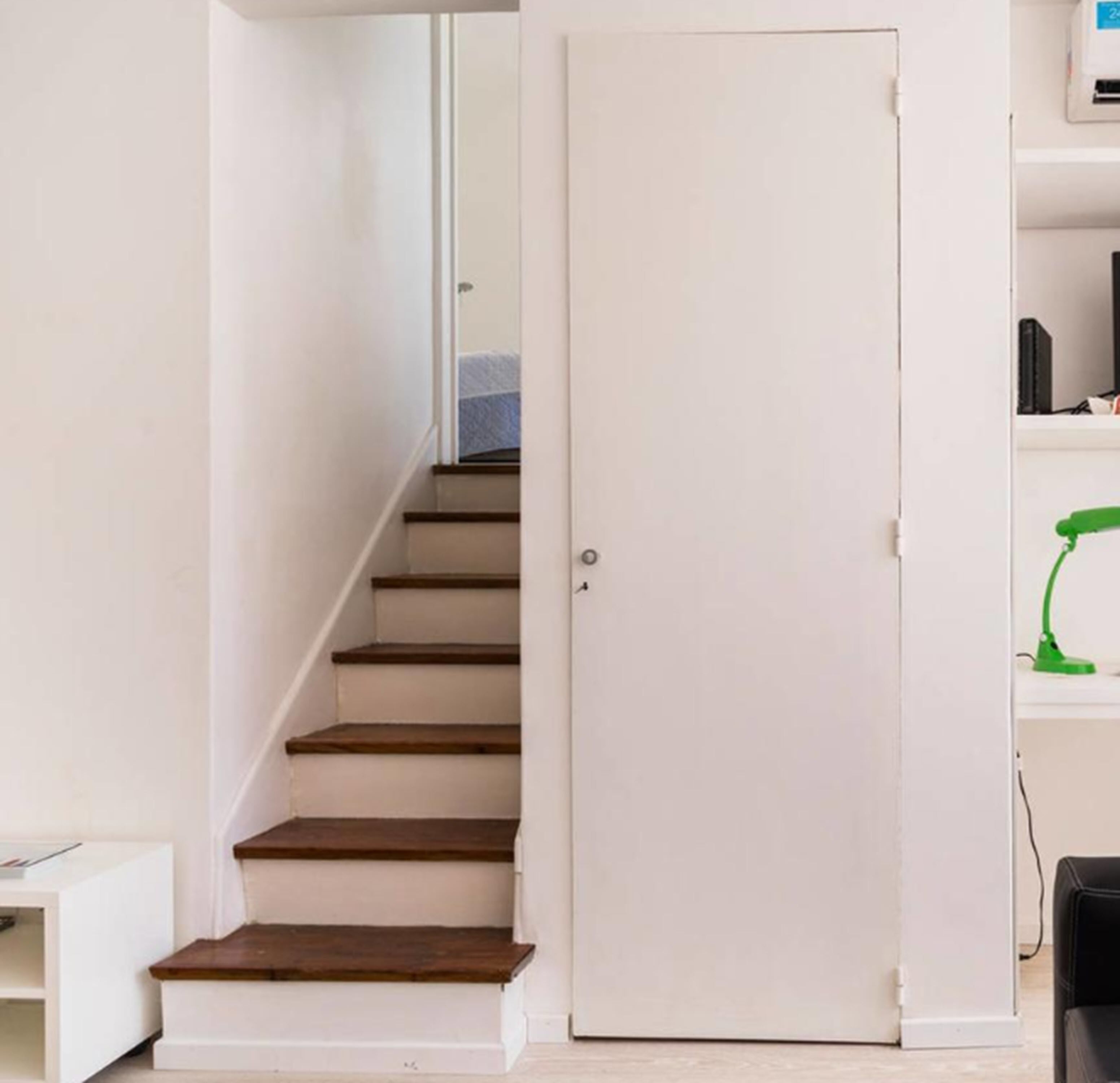 A staircase leading to a door, a desk with a computer, and a green desk lamp.