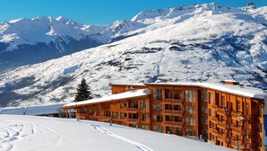 Una cabaña de madera con varios balcones, con las montañas nevadas al fondo.