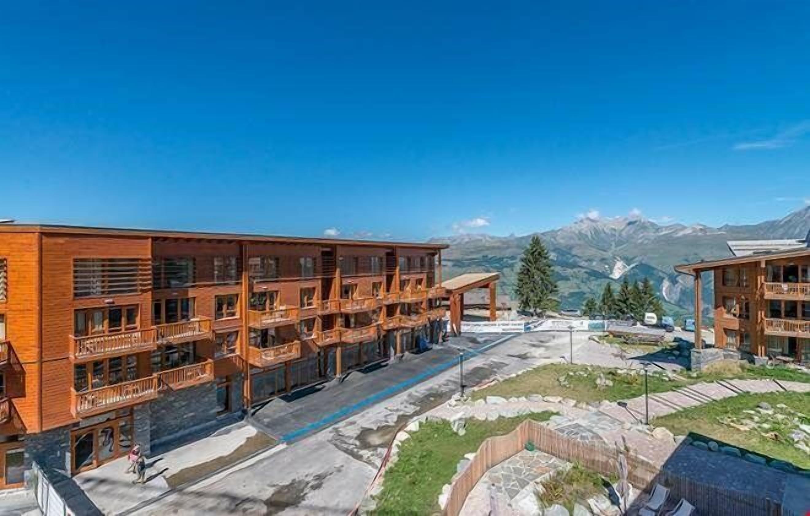Un hotel de varios pisos con balcones, un patio central y un paisaje montañoso de fondo.