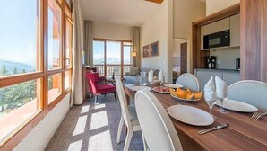 A dining area with a table set for four, a kitchen with a microwave, and a balcony with a view of the mountains.