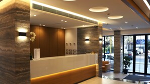 A reception area with a marble reception desk, wooden paneling, and a view of the parking lot through large glass doors. - Alife Apart Hotel (Beirut)