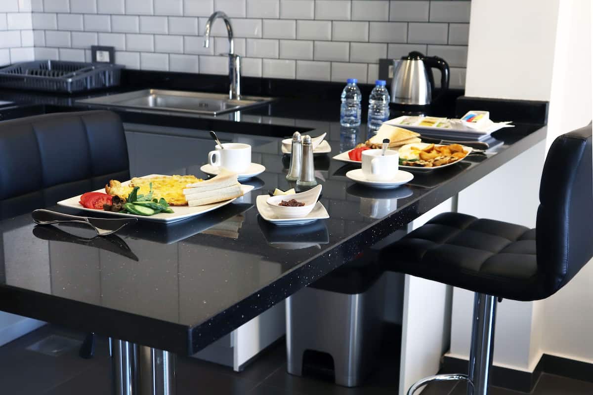 Une cuisine moderne avec un plan de travail noir, des appareils en acier inoxydable et des tabourets de bar noirs.