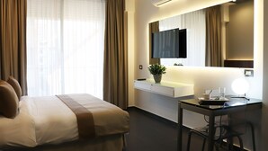 A hotel room with a bed, a desk, a chair, a TV, a plant, and a mirror. - Alife Apart Hotel (Beirut)