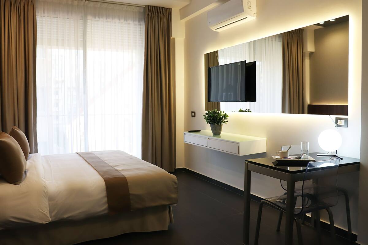 Une chambre d’hôtel avec un lit, un bureau, une chaise, une télévision, une plante et un miroir.