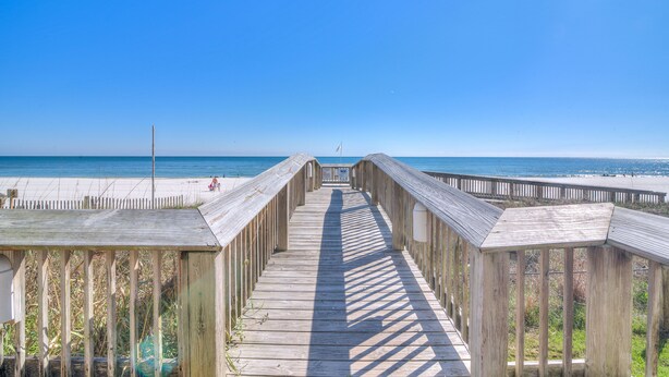 A wooden boardwalk leading to a beach with a clear blue sky.