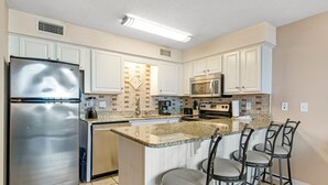 A modern kitchen with white cabinetry, stainless steel appliances, and a central island with bar stools.