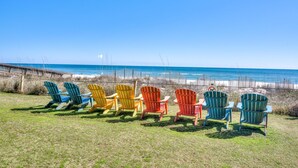 A row of colorful Adirondack chairs facing a beach with a wooden fence and ocean view.