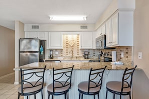 Una cocina con armarios blancos, un refrigerador de acero inoxidable, una encimera de granito y una isla central con taburetes de bar.