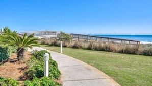 A coastal walkway leading to a beach with a wooden boardwalk and a palm tree.