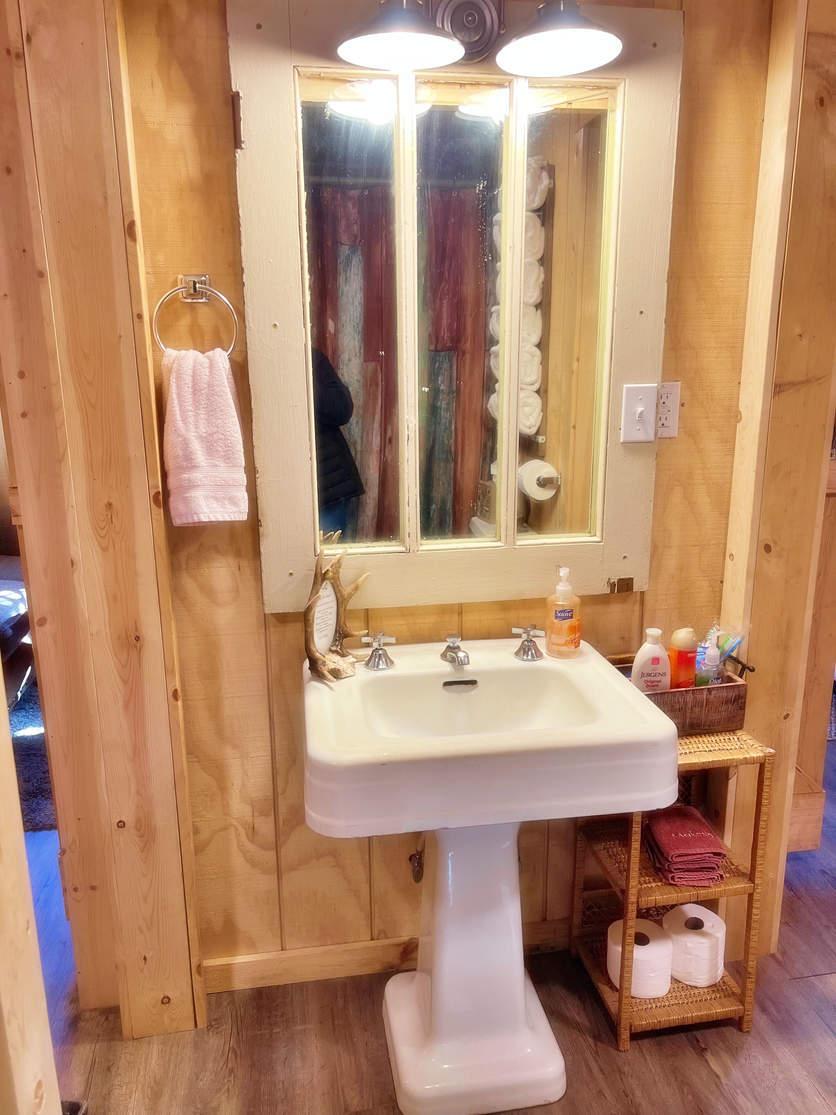 Et badeværelse i træ med en hvid vask, et spejl og en hylde med toiletartikler.