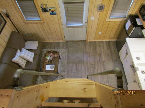 Interno di una baita in legno con un divano, un tavolo con vari oggetti, un fornello e una porta con un cartello.