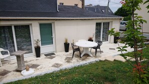 Un patio con una mesa blanca y dos sillas, una planta en maceta y un taburete blanco pequeño.