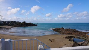 Una playa con costa rocosa, una piscina y una escalera que baja a la playa.