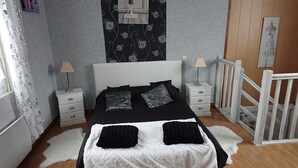 Un dormitorio con cama blanca, almohadas estampadas en blanco y negro, una mesita de noche blanca con lámpara y un aparador blanco.
