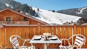 A wooden deck with a table set for two, overlooking a snowy mountain. - Appartement de Montagne | Accès Piscine Extérieure (La Clusaz)