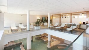 Eine moderne Hotelhalle mit einem Atrium mit Glasboden, Lounge-Sesseln und einer Rezeption.