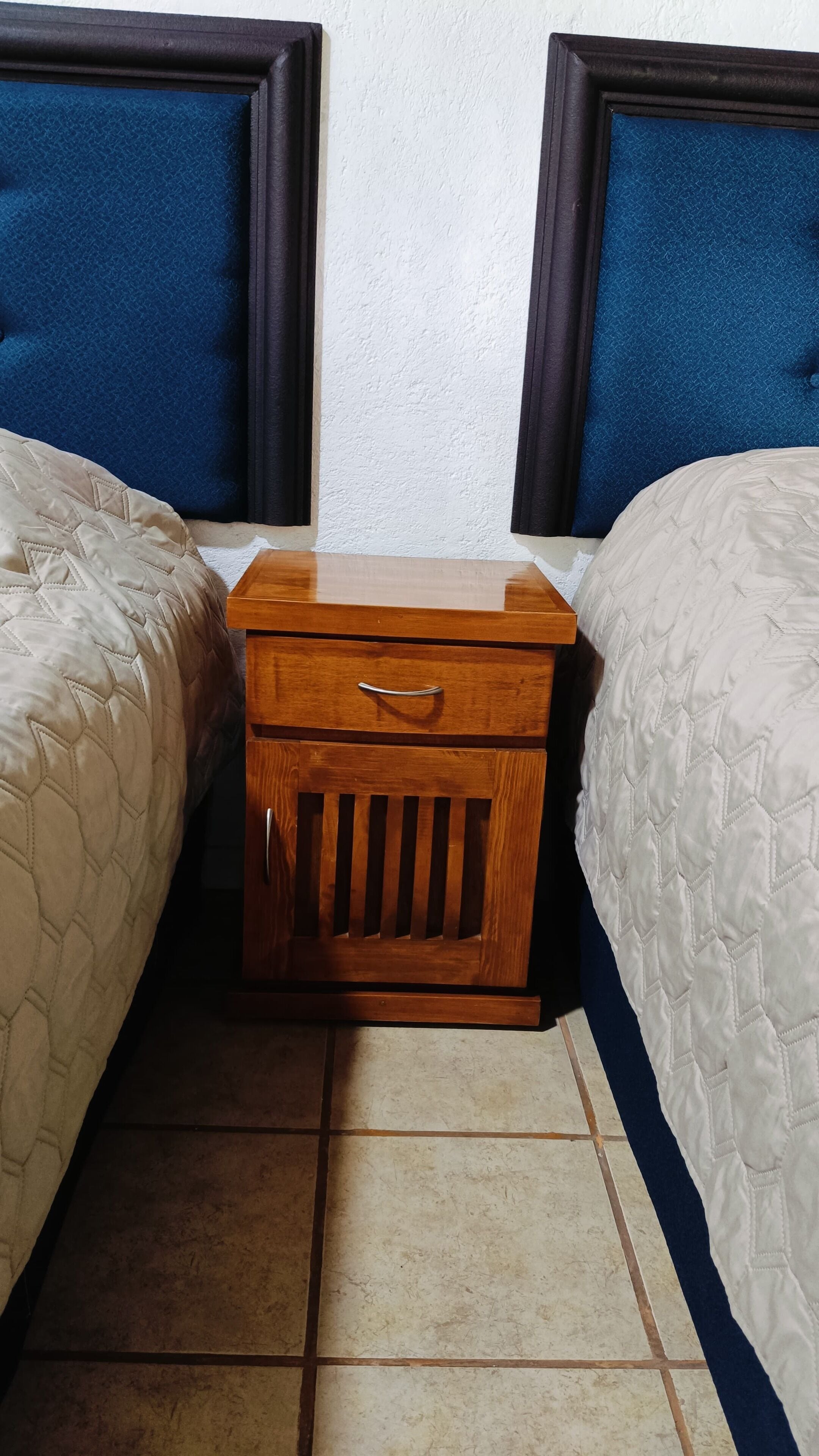 A small wooden nightstand with a drawer between two beds with headboards.