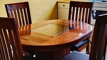 Un coin repas avec une table et des chaises en bois, une cuisine à l’arrière-plan et une fenêtre avec des rideaux.