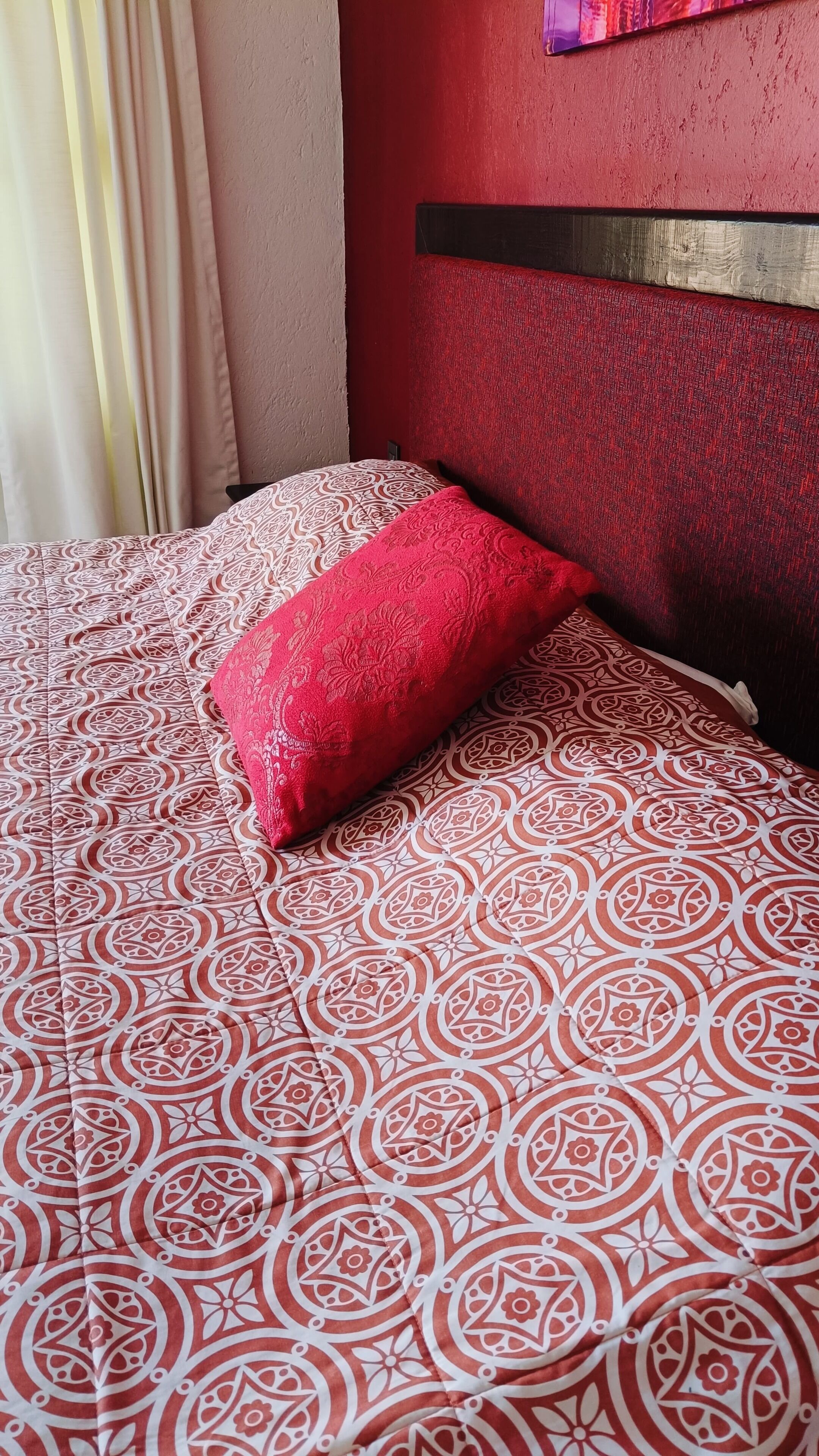 Un lit avec une couvre-lit à motifs et un seul oreiller rouge.