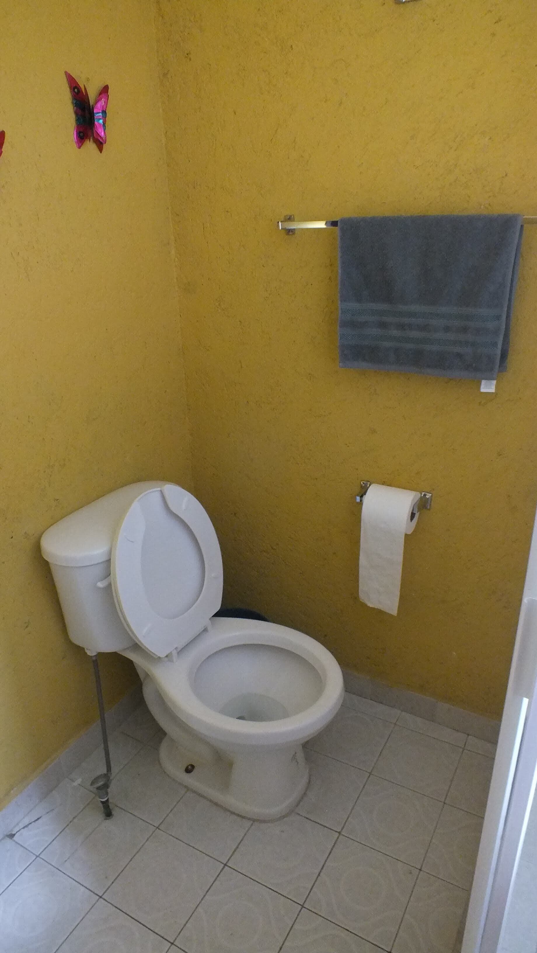 Um banheiro pequeno com vaso sanitário branco, uma toalha pendurada em um suporte de metal e um rolo de papel higiênico.