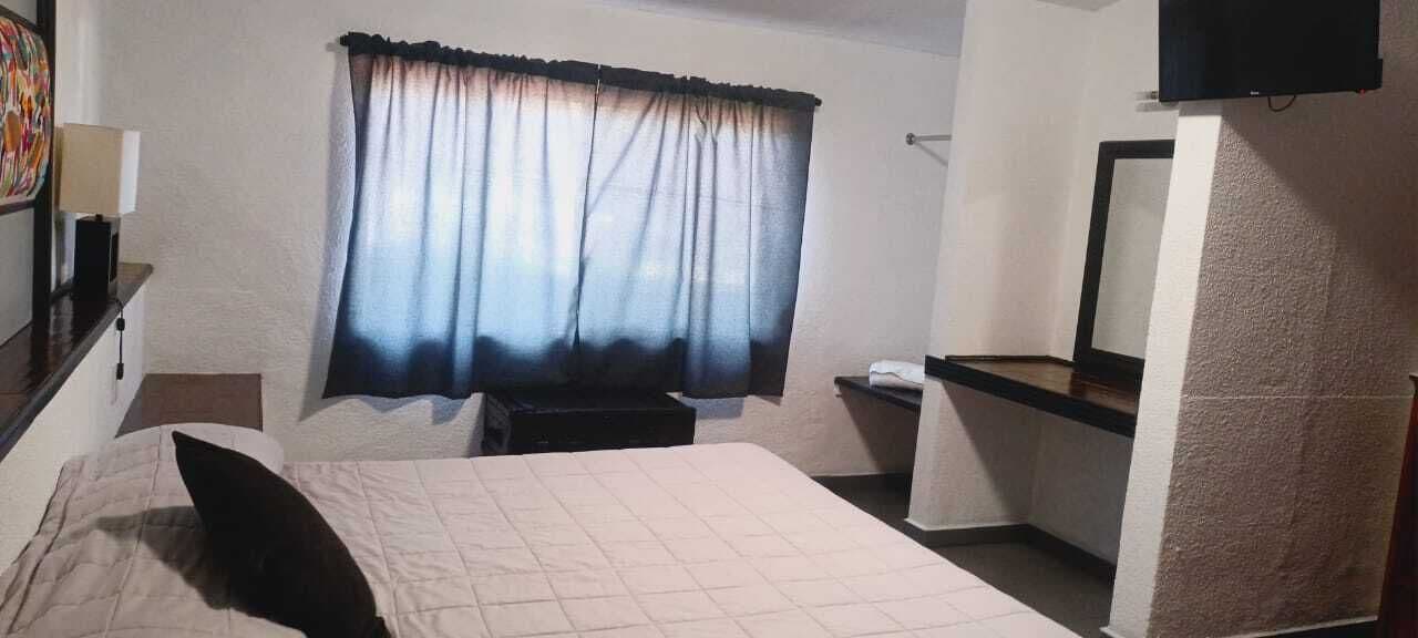 Een hotelkamer met een bed, een bureau, een stoel, een televisie en een raam met gordijnen.