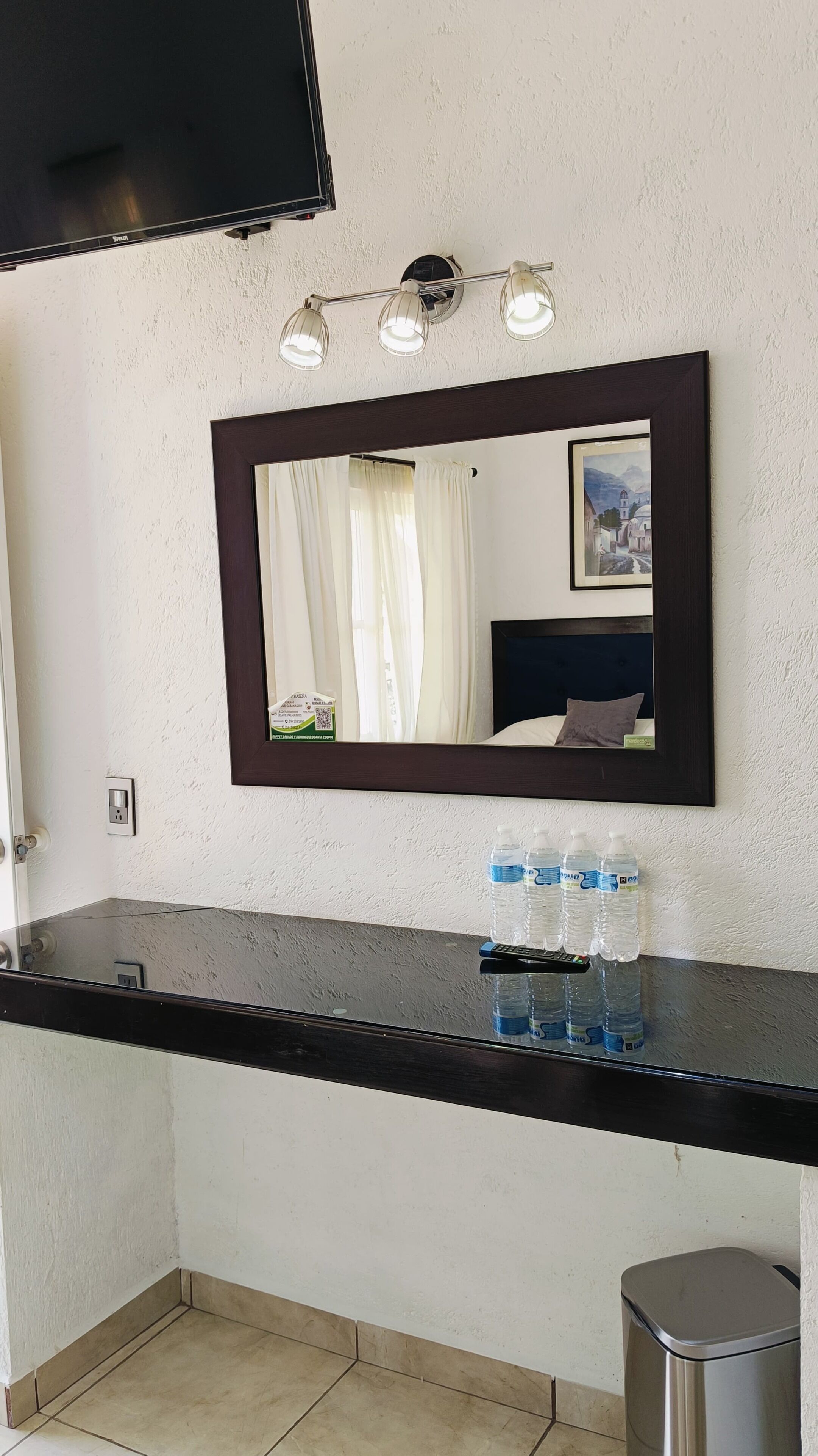 Un baño de hotel con encimera negra, espejo, lavamanos y cubo de basura.