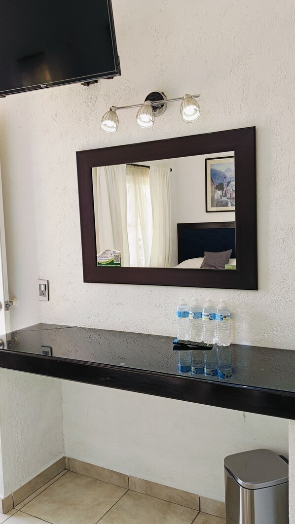 A hotel bathroom with a black countertop, a mirror, a sink, and a trash bin.
