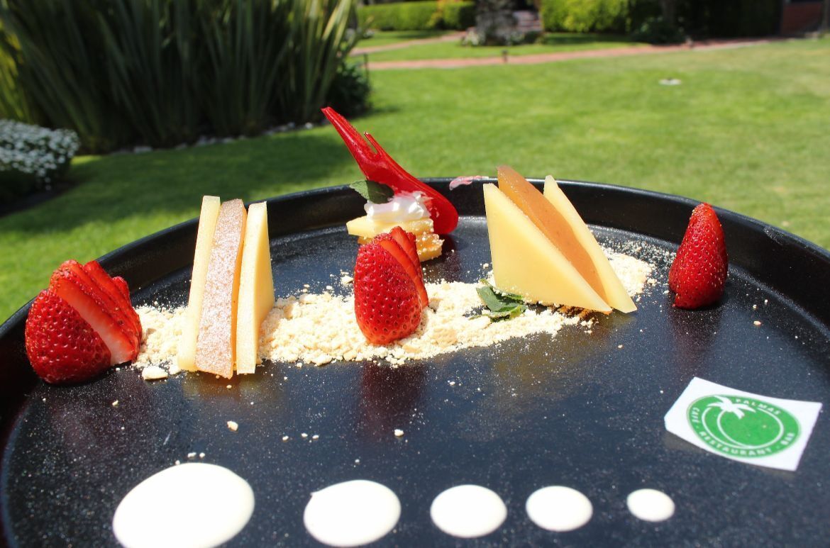 A dessert plate with strawberries, cream, and cake slices on a black plate with a logo.
