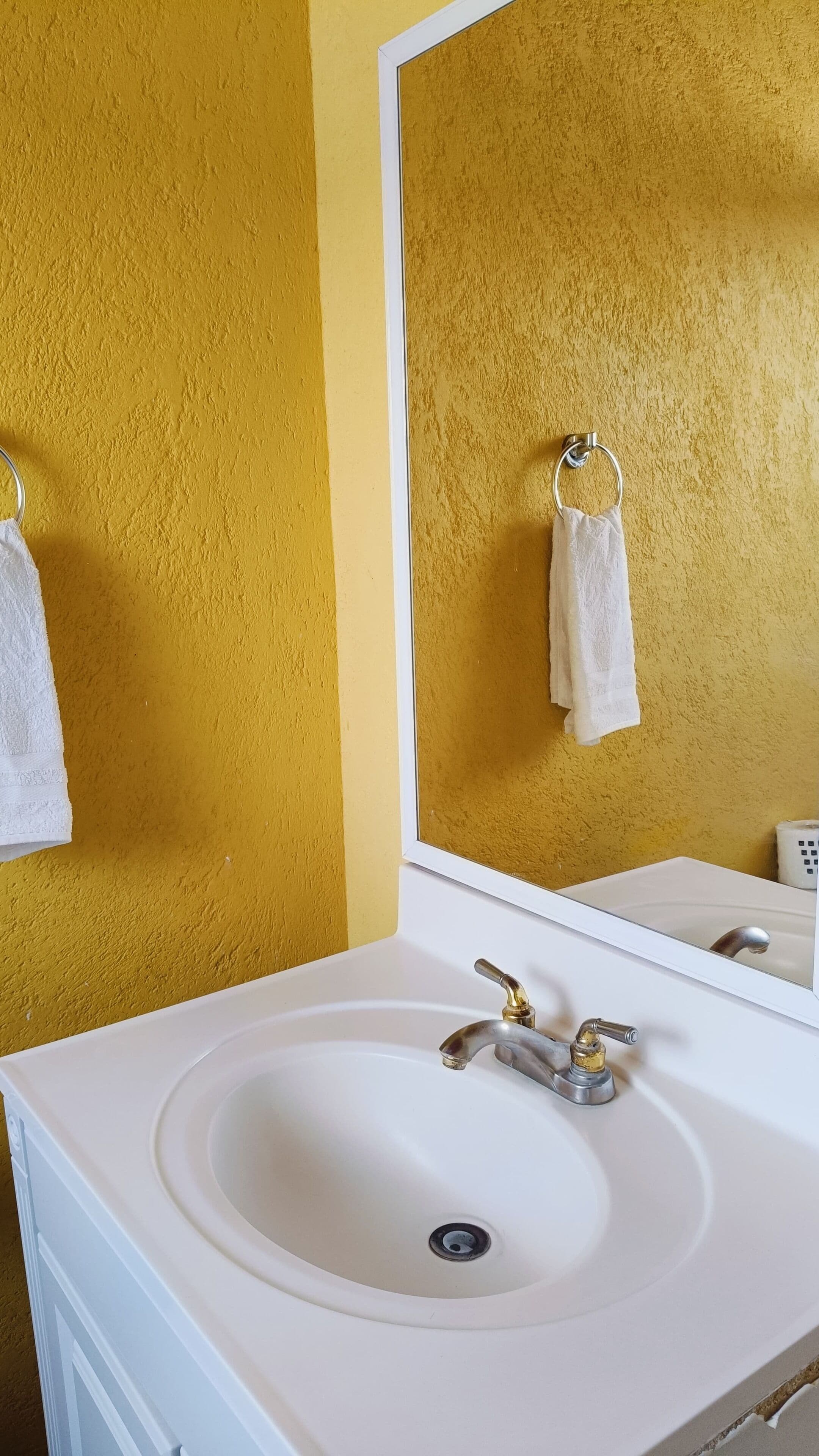 Une salle de bain avec un lavabo blanc, des murs de couleur or et un miroir au-dessus du lavabo.