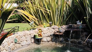 Ein klares Teichgewässer mit einer Steinmauer, einem kleinen Wasserfall und Zierfiguren.